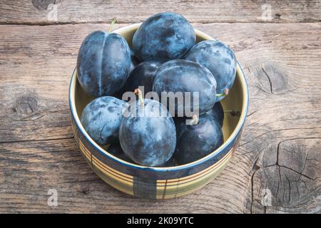 Keramikschale voller frisch gepflückter Pflaumen auf Holztisch. Süße Bio-Früchte kultiviert zu Hause im Garten ohne Düngung. Prunus Domestica. Stockfoto