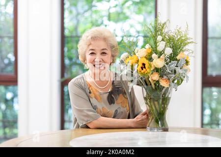 Glückliche ältere chinesische Frau, die zu Hause Blumen arrangiert Stockfoto