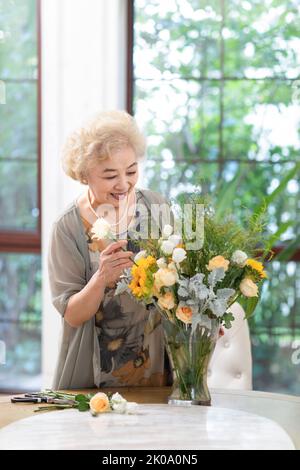 Glückliche ältere chinesische Frau, die zu Hause Blumen arrangiert Stockfoto