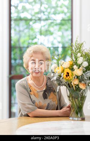 Glückliche ältere chinesische Frau, die zu Hause Blumen arrangiert Stockfoto