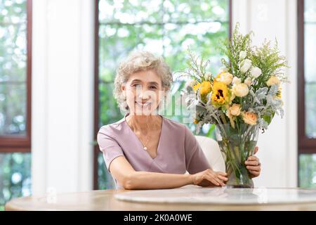 Glückliche ältere chinesische Frau, die zu Hause Blumen arrangiert Stockfoto