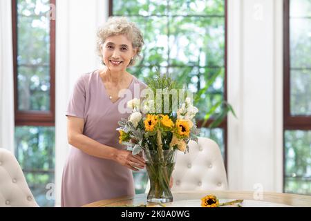 Glückliche ältere chinesische Frau, die zu Hause Blumen arrangiert Stockfoto