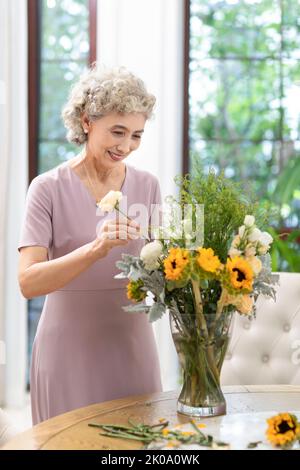 Glückliche ältere chinesische Frau, die zu Hause Blumen arrangiert Stockfoto