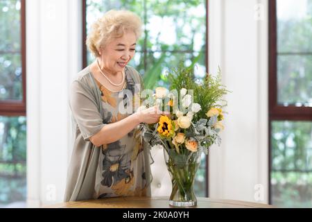 Glückliche ältere chinesische Frau, die zu Hause Blumen arrangiert Stockfoto
