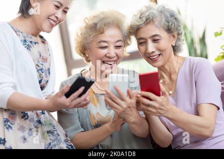 Glückliche ältere chinesische Freunde, die zu Hause Smartphones benutzen Stockfoto