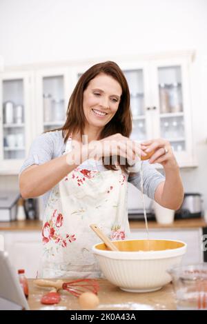 Das Eiweiß vom Eigelb trennen. Eine reife Frau bricht in der Küche ein Ei. Stockfoto