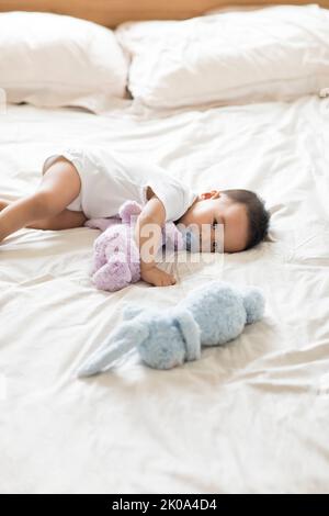 Niedliches chinesisches Baby, das mit Schnuller auf dem Bett liegt Stockfoto