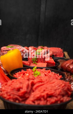 Gemischtes rohes Rindfleisch mit dunklem Ziegelwand Hintergrund Seitenansicht Stockfoto