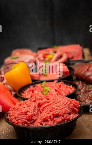 Gemischtes rohes Rindfleisch auf dem Tisch mit Seitenansicht im schwarzen Hintergrund Stockfoto