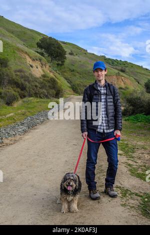 Mann, der in Oakland, Kalifornien, mit einem Hund durch einige Hügel läuft Stockfoto