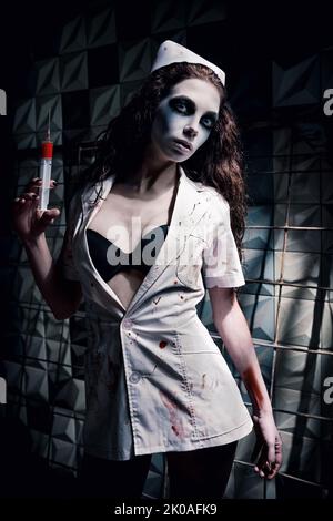 Horrorfoto: Die seltsame gruselige Krankenschwester (Arzt) in blutiger Uniform, mit Spritze in der Hand. Zombie-Frau (lebend tot) Stockfoto