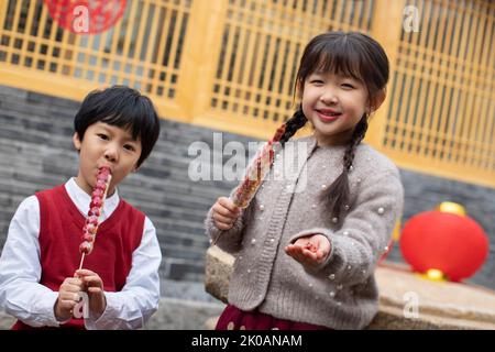 Glückliche chinesische Geschwister essen kandierte Hagebutten Stockfoto