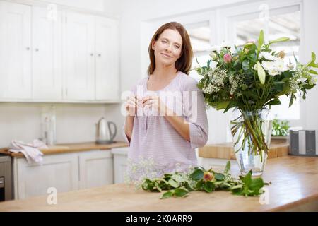 Der Duft frischer Blumen lässt sie immer träumen. Eine schöne Frau, die zu Hause einen Blumenstrauß arrangiert. Stockfoto