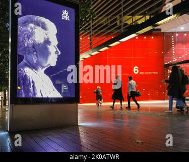 London, Großbritannien. 10. September 2022. In London Bridge City in Southwark laufen die Menschen auf dem Bürgersteig entlang, während ein Bild der Königin in ihre Richtung zu schauen scheint. Die beleuchtete Tafel mit einem schwarz-weißen Foto des Monarchen ist eine öffentliche Hommage nach dem Tod von Königin Elizabeth II.. Kredit: Imageplotter/Alamy Live Nachrichten Stockfoto