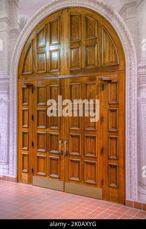Große gewölbte Doppeltür in der Kirche in der Innenstadt von Tucson, Arizona. Kircheneingang mit rotem Fliesenboden und dekorativem Türrahmen. Stockfoto