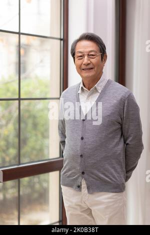 Älterer Chinese, der vor dem Fenster steht Stockfoto