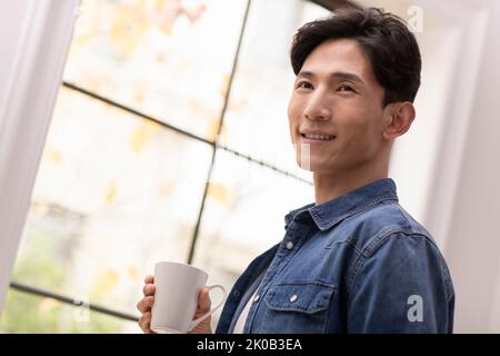 Glücklicher junger Chinese, der Kaffee hält Stockfoto