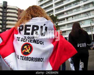 Eine Frau mit einer peruanischen Flagge auf ihrem Rücken, die lautet: „Peru, ich liebe dich, Deshalb verteidige ich dich und ein durchgestrichenes kommunistisches Symbol, wenn Hunderte sich auf den Straßen versammeln, um den 30.. Jahrestag der Gefangennahme und den ersten Jahrestag des Todes von Abimael Guzman, dem Anführer der Terrorgruppe Shining Path, zu feiern. Guzman (86) wurde am 12.. September 1992 festgenommen und starb am 11.. September 2021 im Gefängnis der Marinestützpunkt Callao, wo er wegen terroristischer Handlungen, die das Land in den Jahren 1980s und 1990s verwüstet hatten, eine lebenslange Haftstrafe verbüßte. Stockfoto