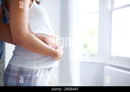 Fruchtbare Anfänge - Copyspace. Seitenansicht einer jungen Frau, die im Bauch schwanger ist und von ihr und ihrem Freund gehalten wird. Stockfoto