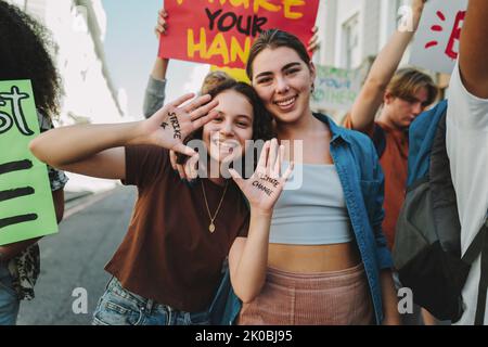 Globaler Streik für den Klimawandel. Glückliche Teenager-Mädchen lächeln der Kamera zu, während sie mit einer Gruppe von Demonstranten gegen die globale Erwärmung marschieren. Jugendac Stockfoto