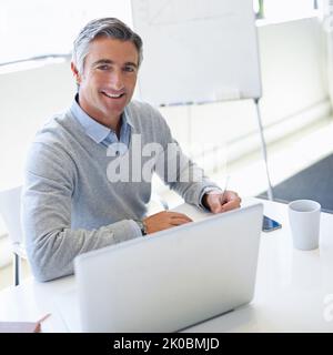 In dieser Branche arbeiteten immer bis zu einem Termin. Porträt eines reifen Geschäftsmannes, der im Büro an seinem Laptop arbeitet. Stockfoto
