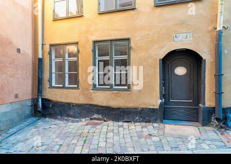 Vintage verzierte Holztür und zwei Holzfenster in einer grunge gelben Wand an der Straße mit Kopfsteinpflaster-Boden, Altstadt, Stockholm, Schweden Stockfoto