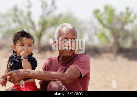 Portrait Foto von Indian Senior Großvater mit Kleinkind Enkel siting in der Natur und spielen im Freien , Rajasthan Indien Stockfoto