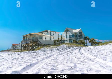 Strandhäuser auf einem weißen Sand an einem Strand in Destin, Florida. Es gibt Strandhäuser mit Säulen und Terrasse vor dem klaren blauen Himmel Hintergrund. Stockfoto