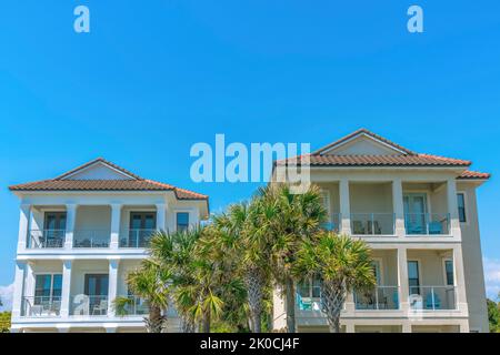 Destin, Florida- Fassade von zwei Strandhäusern mit Palmen in der Mitte. Außenansicht von Strandhäusern mit Balkonen vor dem Hintergrund des blauen Himmels. Stockfoto
