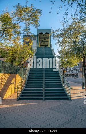 Phoenix, Arizona - Treppe einer Fußgängerbrücke mit Landungen und Geländern. Fußgängerbrücke Treppe in der Nähe der Wand auf der linken Seite und Bäume auf der rechten Seite in der Nähe der ro Stockfoto