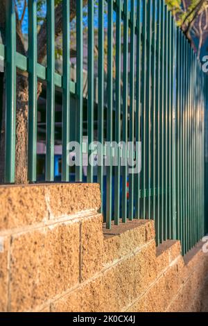 Nahaufnahme einer Betonblockwand mit lackierten grünen Geländern - Phoenix, Arizona. Selektiver Fokus einer Zaunwand mit Metallgeländern über dem Beton Stockfoto