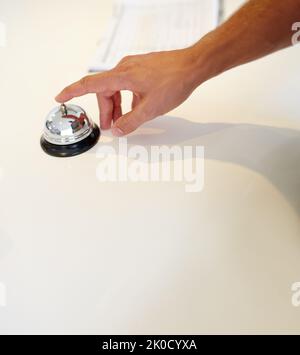 Klingelt in seinem Urlaub. Eine Hand klingelt eine Glocke an einem Check-in-Schalter des Hotels. Stockfoto