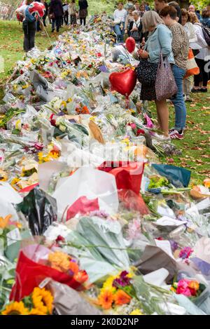 Nach dem Tod von Königin Elizabeth II. Halten Menschen inne, um Botschaften auf den Blumenhügeln im Green Park zu lesen Weibchen betrachten Blumengebete Stockfoto