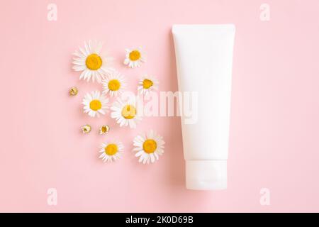 Mockup weiße Squeeze-Flasche kosmetische Tube, blühende medizinische Chamomilles Daisy auf rosa Hintergrund. Körpercreme, Gel, Hautpflege, Sonnencreme, Feuchtigkeitscreme. Stockfoto