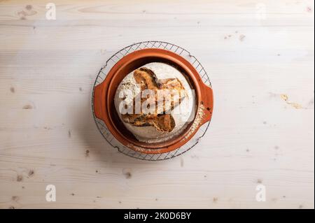 Draufsicht auf köstliche Bio hausgemachtes Sauerteig Brot frisch gebacken in Tontopf auf Holz Hintergrund platziert. Stockfoto
