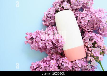 Mockup weiße kosmetische Tube Flasche mit rosa Schraubverschluss und lila Blüten auf blauem Hintergrund. Körpercreme, Gel, Hautpflege, Sonnencreme, Feuchtigkeit Stockfoto