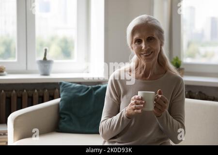 Glückliche ältere Dame, die zu Hause Tee trinkt und guten Morgen genießt Stockfoto