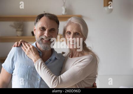 Fröhliches, liebevolles Seniorenpaar umarmt sich und schaut in die Kamera Stockfoto