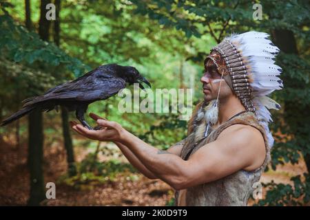 Ein Mann in traditioneller indianischer Kleidung, der eine Krähe in der Hand hält Stockfoto