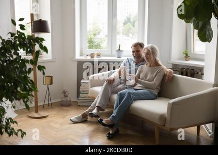 Glückliches Rentnerpaar, das auf der Couch im neuen Zuhause sitzt Stockfoto