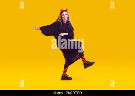 Furchterregend tanzende emotionale Frau mit offenem Mund, gekleidet als verrückter Teufel für Halloween. Stockfoto