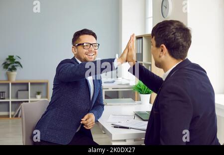 Zwei Kollegen geben sich gegenseitig hohe fünf, um ihre Arbeit zu feiern, die gut gemacht und erfolgreich abgeschlossen wurde. Stockfoto