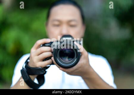 Der asiatische Mann hält die Mittelformatkamera in der Hand und fokussiert, um vor ihm zu fotografieren. Stockfoto