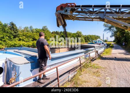 Ein Bargeman beobachtet an einem sonnigen Sommertag die Beladung seines motorisierten Lastkahnes, der auf einem Kanal in einem Sandsteinbruch festgemacht ist, mit Kies. Stockfoto