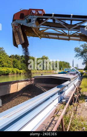 An einem sonnigen Sommertag wird eine motorisierte Barge, die auf einem Kanal festgemacht ist, in einem Sandsteinbruch mit Kies beladen. Stockfoto