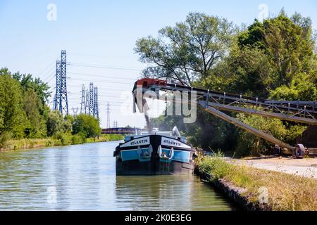 An einem sonnigen Sommertag wird eine motorisierte Barge, die auf einem Kanal festgemacht ist, in einem Sandsteinbruch mit Kies beladen. Stockfoto