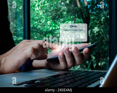 Zwei Schritte Authentifizierung oder 2FA Konzept. 2023 Verifizierungscode mit Schlüsselsymbol auf dem Smartphone-Bildschirm in der Hand mit Laptop zur Kennwortvalidierung Seite, ID Stockfoto