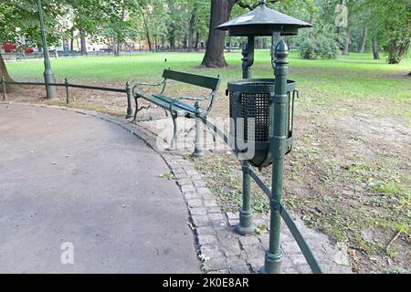 Eine Metallbank und ein Mülleimer in einem Park in der polnischen Stadt Krakau. Stockfoto