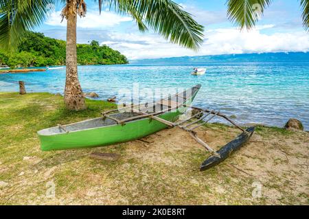 Ein altes Auslegboot, das zur Navigation von Insel zu Insel in Fidschi verwendet wurde, liegt an der sandigen Küste, eingerahmt von einem wunderschönen blauen Himmel und Ozean. Stockfoto