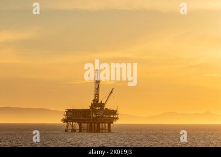 Dramatisches Bild einer Offshore-Ölplattform vor der Küste Kaliforniens vor einem gelben Winterhimmel, wenn die Sonne untergeht. Stockfoto